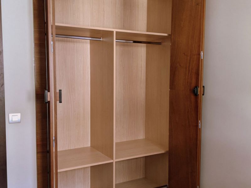 Armario de madera clara con puertas correderas plegables abierto