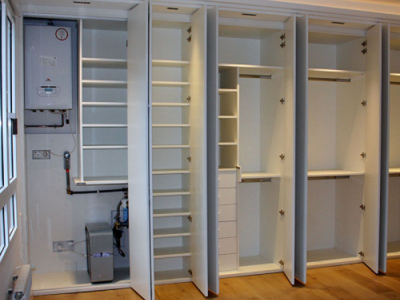 Armario de puertas enrasadas abierto, de color blanco y múltiples compartimentos