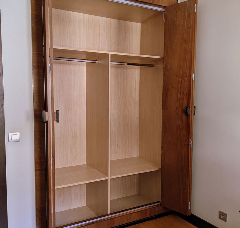 Armario de madera clara con puertas correderas plegables abierto